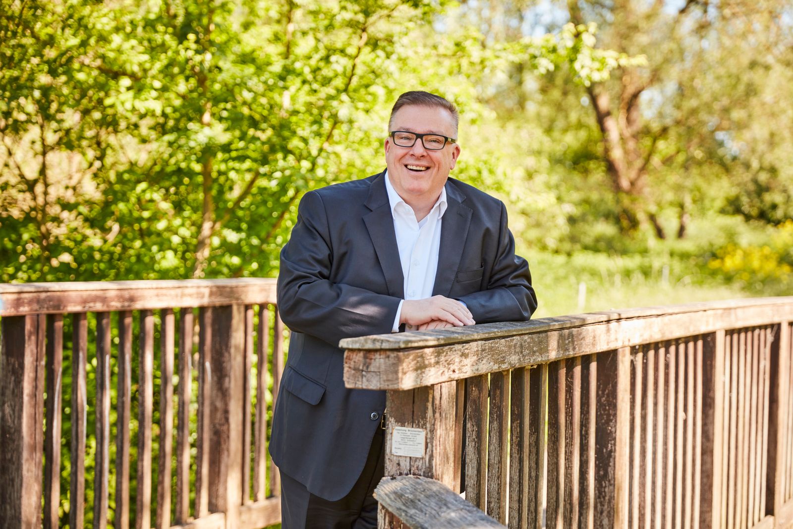 Andreas Ruck lachend an einer Holzbrücke im Grünen.
