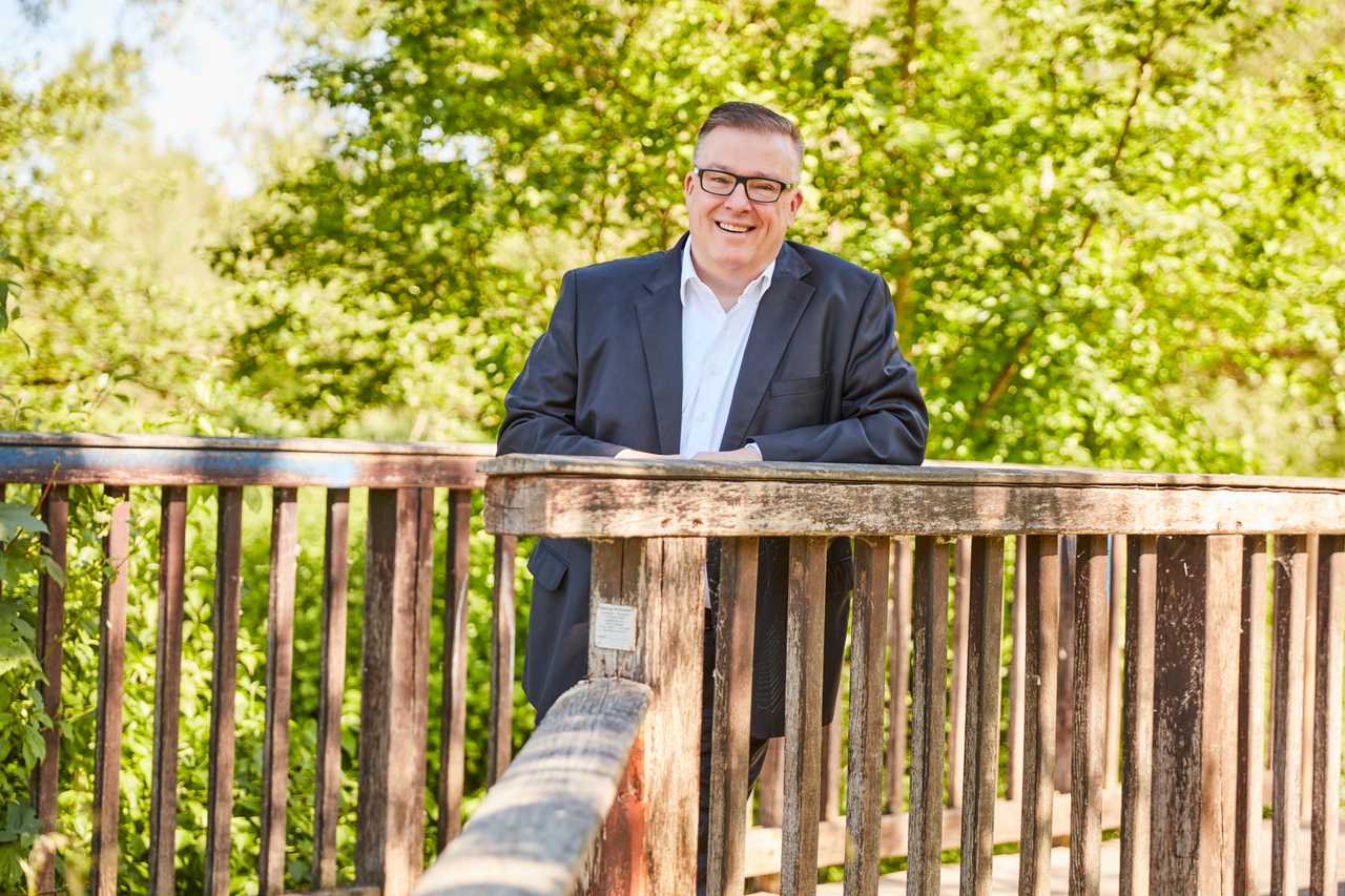 Andreas Ruck lachend an einer Holzbrücke.