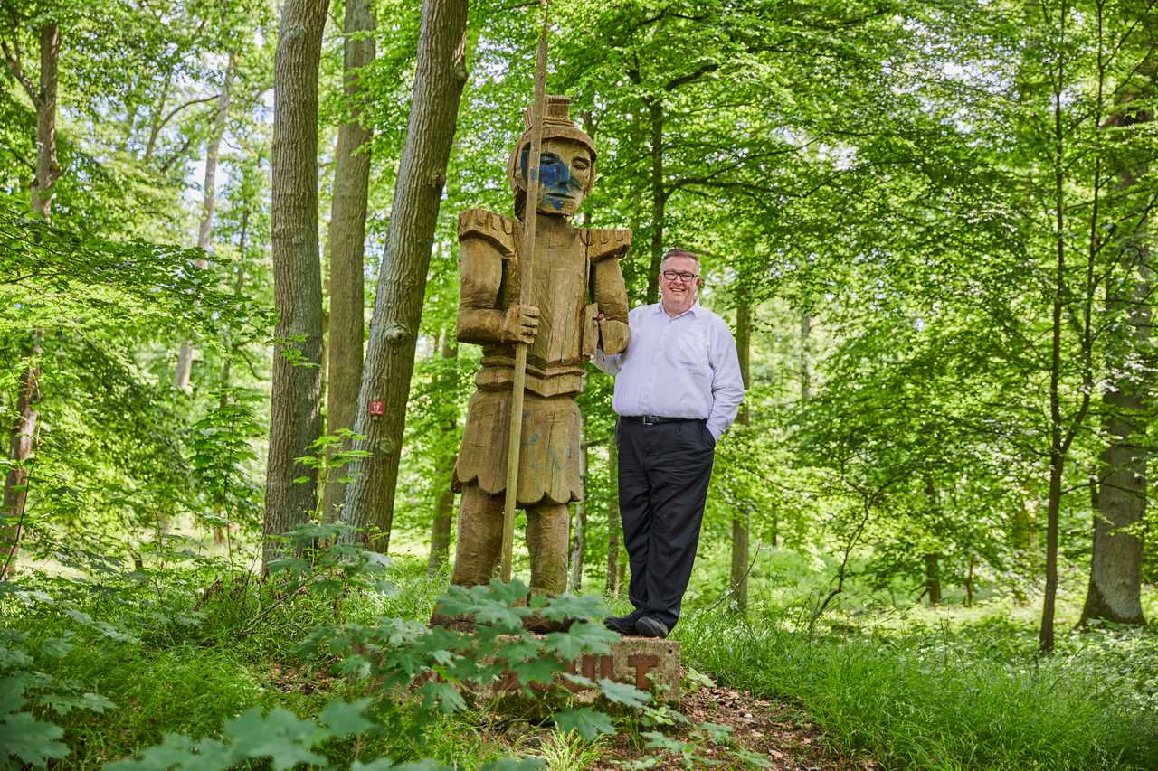 Andreas Ruck neben einer Holzfigur im Wald.