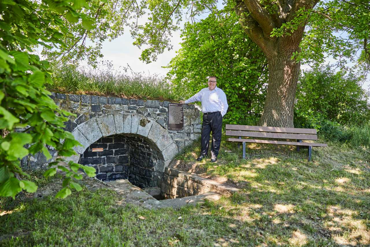 Andreas Ruck an einer alten Steinbrücke unter Bäumen.