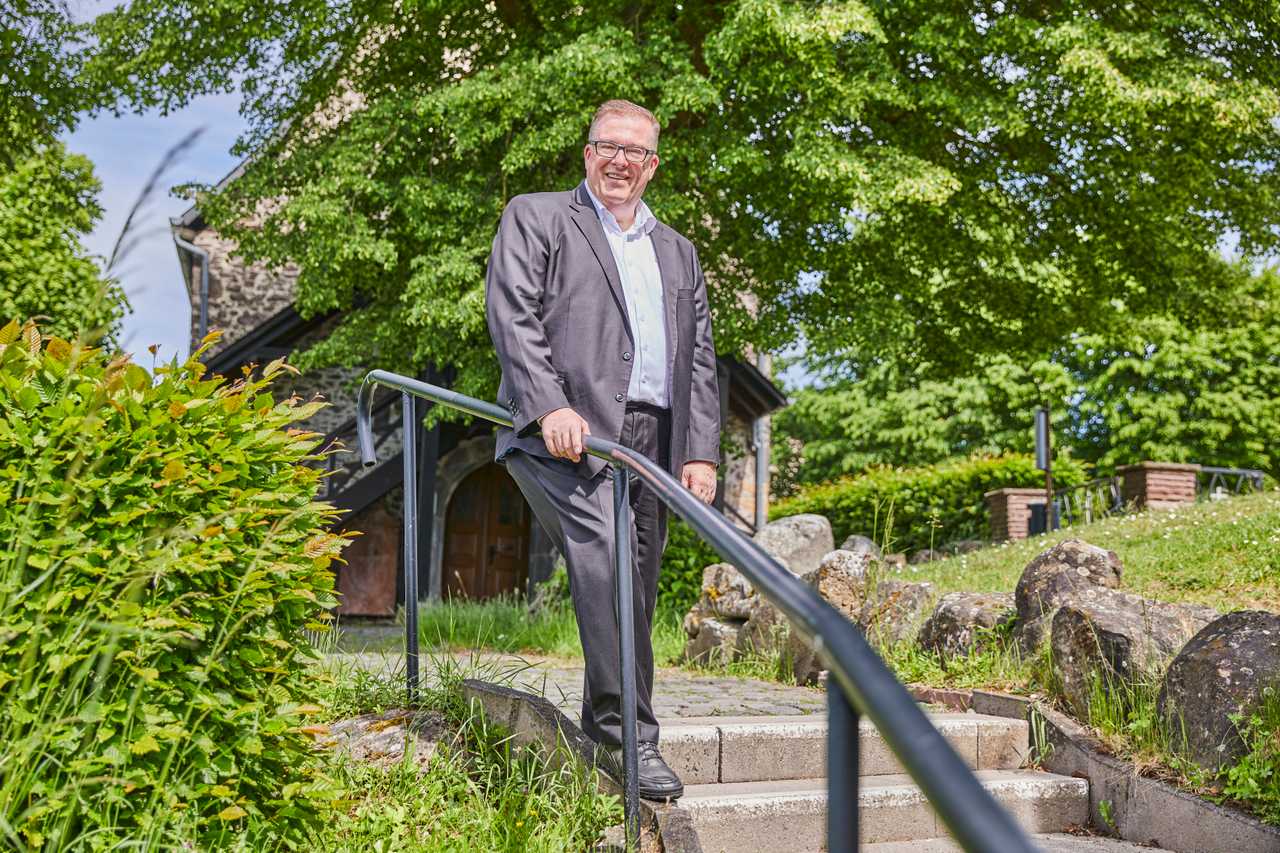 Andreas Ruck auf einer Treppe vor einem historischen Gebäude im Grünen.